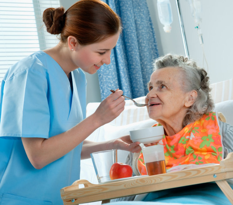 senior woman lying in bed while a caregiver serving food
